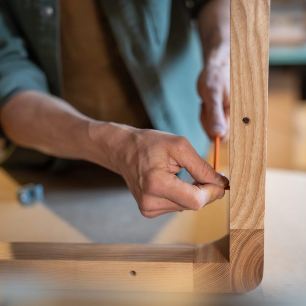Male craftsman screwing furniture screws into the table, joins the pieces together, hands using hex wrench closeup. Creating furniture for home, customised work. Carpentry workshop.
